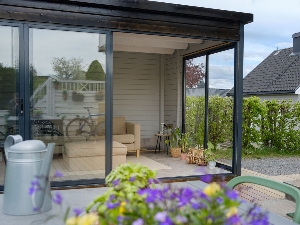 sort anneks med store vindusflater og blomster i forkant