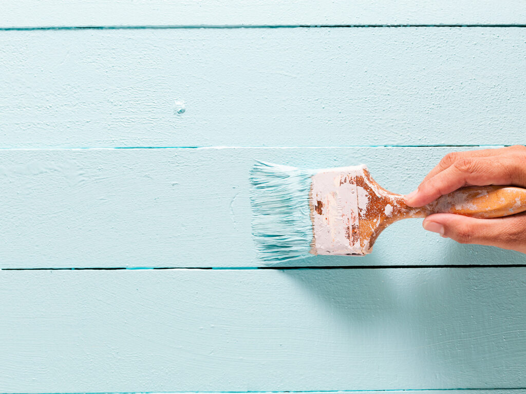 hånd som holder malepensel med turkis maling på vegg