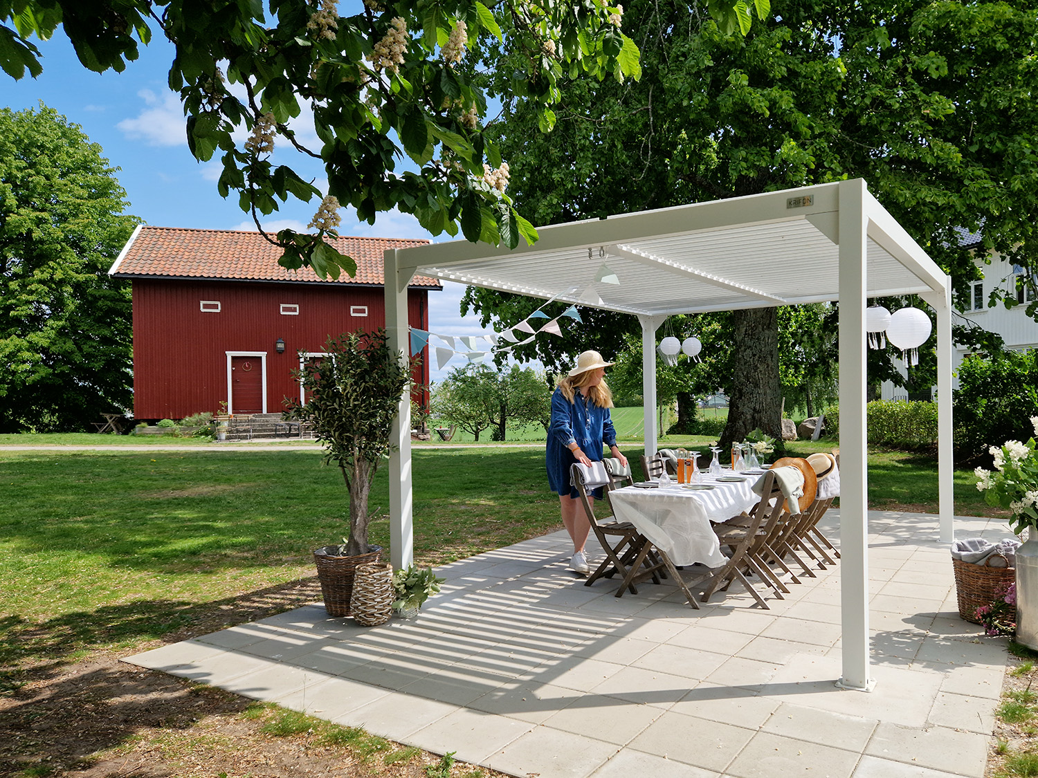 dame i stråhatt dekker bord under en hvit pergola