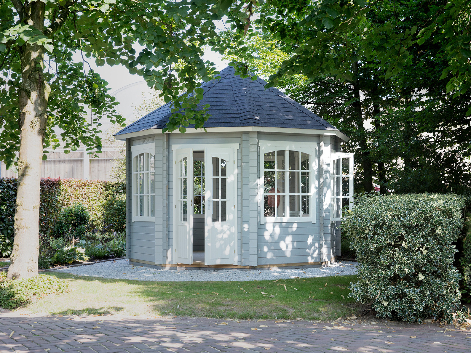 Grått lysthus i en hage med grønne trær. Bilde.