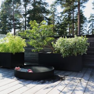 Sorte plantekasser med blomster og planter med et vannspeil foran. Foto